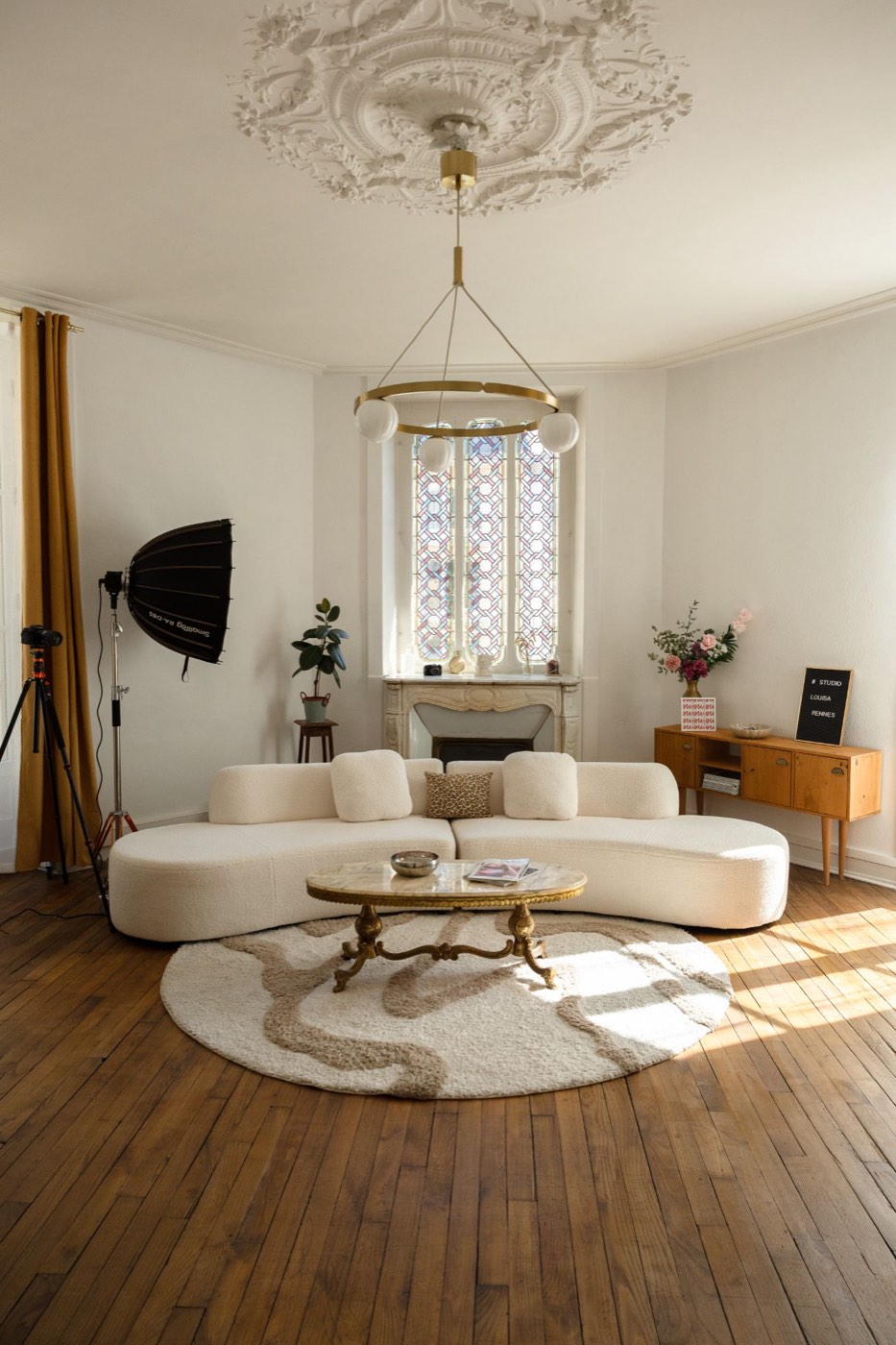 Salon haussmannien du Studio Louisa à Rennes : canapé arrondi en bouclette, vitrail et lustre doré